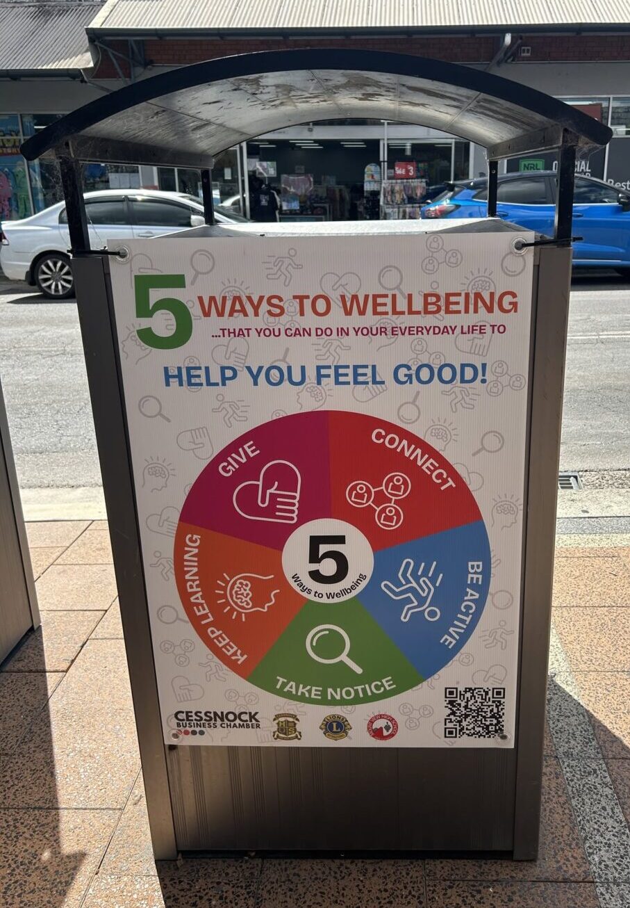 A 5 Ways to Wellbeing sign on a Cessnock street, showing the wheel of Connect, Be Active, Take Notice, Keep Learning and Give